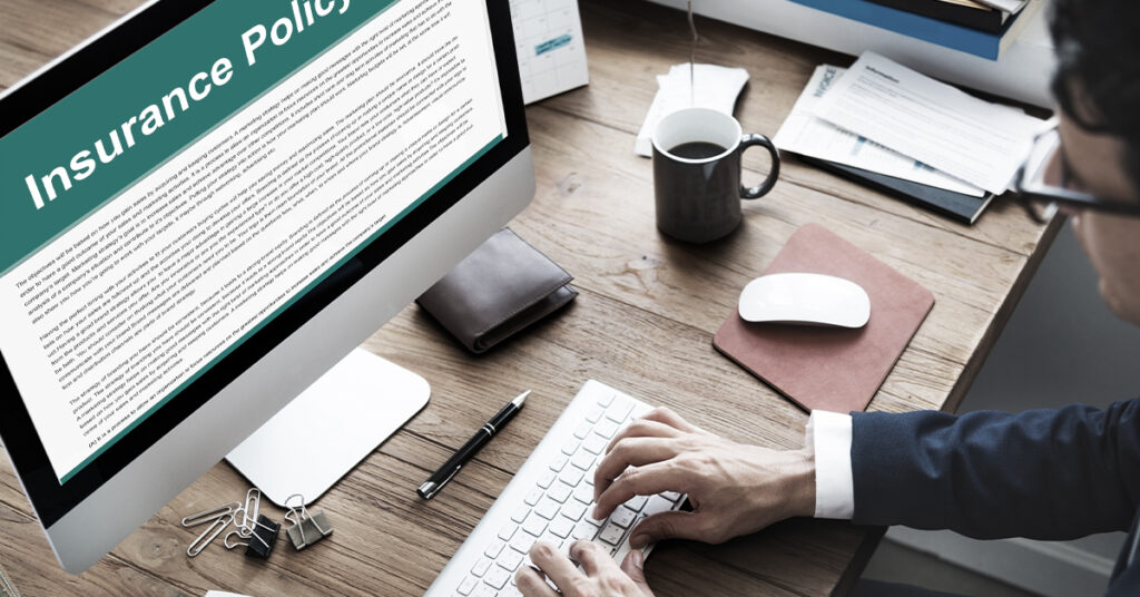 A person reviews an insurance policy on a desktop computer at a modern office desk.