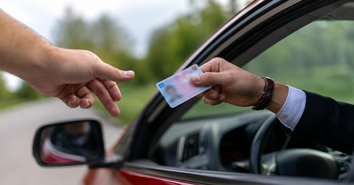 Driver handing over a blurred license from a car window, reminding that driving without a license is illegal.