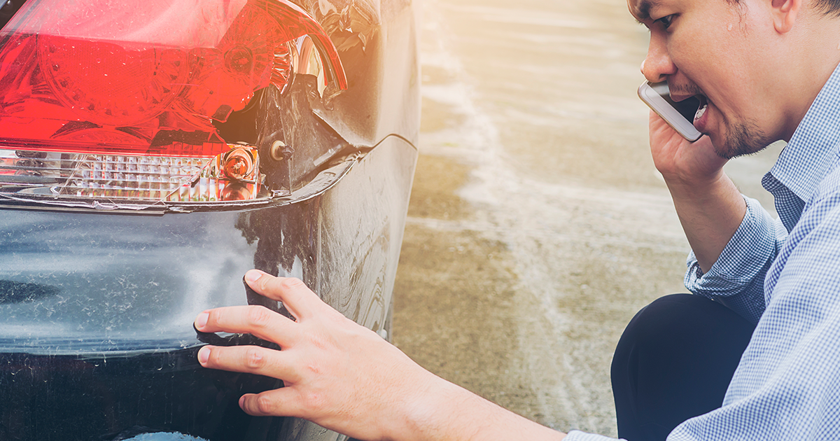 Man calling after a car accident while inspecting the rear bumper damage.