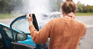 Woman holding her neck beside a smoking car after an accident.