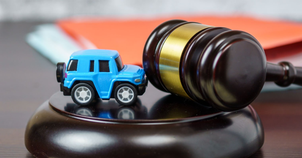 Toy car beside a judge’s gavel on a desk.