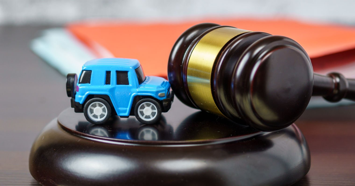 Toy car beside a judge’s gavel on a desk.