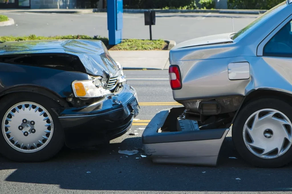 Close-up of a front-end collision showing a black car with a crushed hood and a silver car with a detached rear bumper.