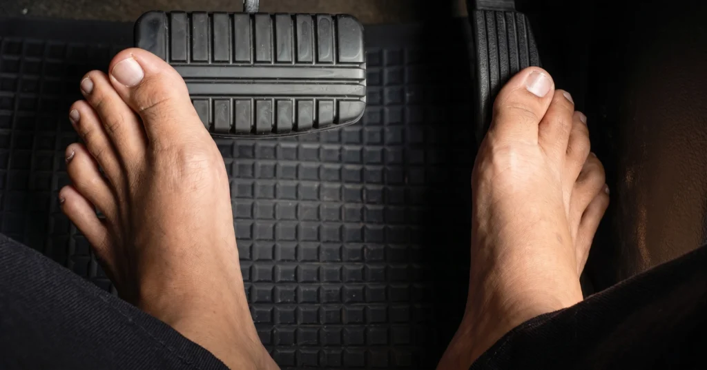 Bare feet pressing the brake and gas pedals inside a car.