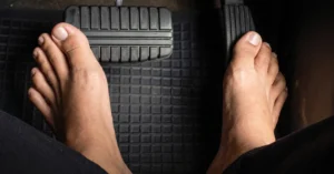 Bare feet pressing the brake and gas pedals inside a car.