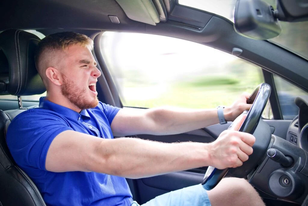 Side view of a stressed driver shouting and gripping the steering wheel while driving recklessly.