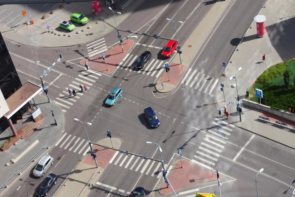 A high-angle view of a city intersection with vehicles driving and pedestrians crossing the street.