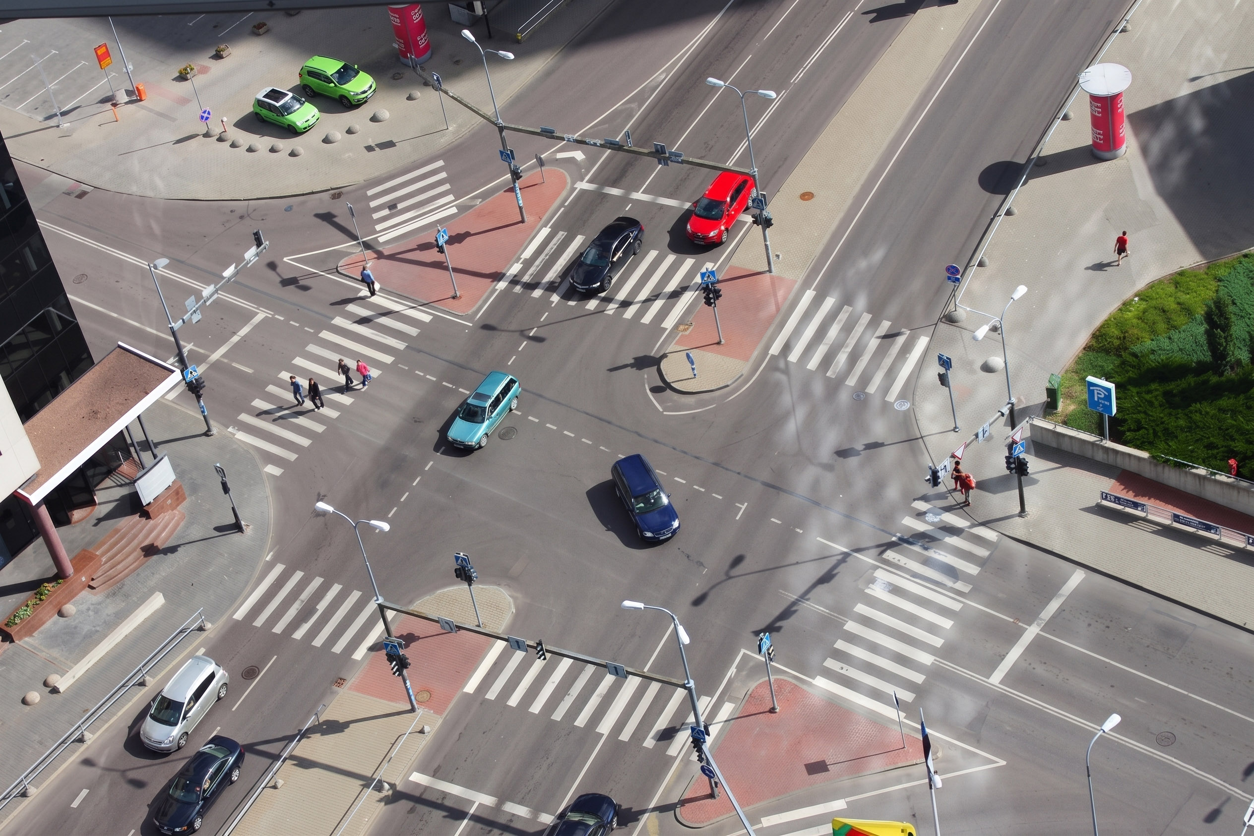 A high-angle view of a city intersection with vehicles driving and pedestrians crossing the street.