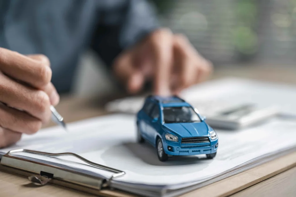 Close-up of a man shaking hands with an insurance agent holding a clipboard in front of two collided cars.