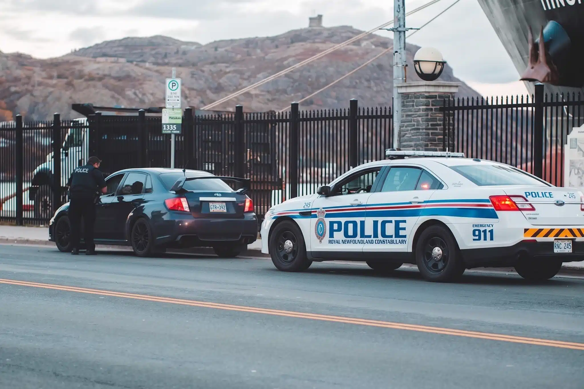 A Royal Newfoundland Constabulary police officer conducting a traffic stop of a dark sedan on a roadside