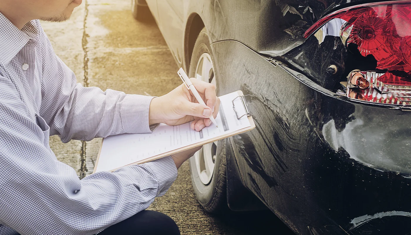 Insurance adjuster writing notes on clipboard inspecting damaged car bumper